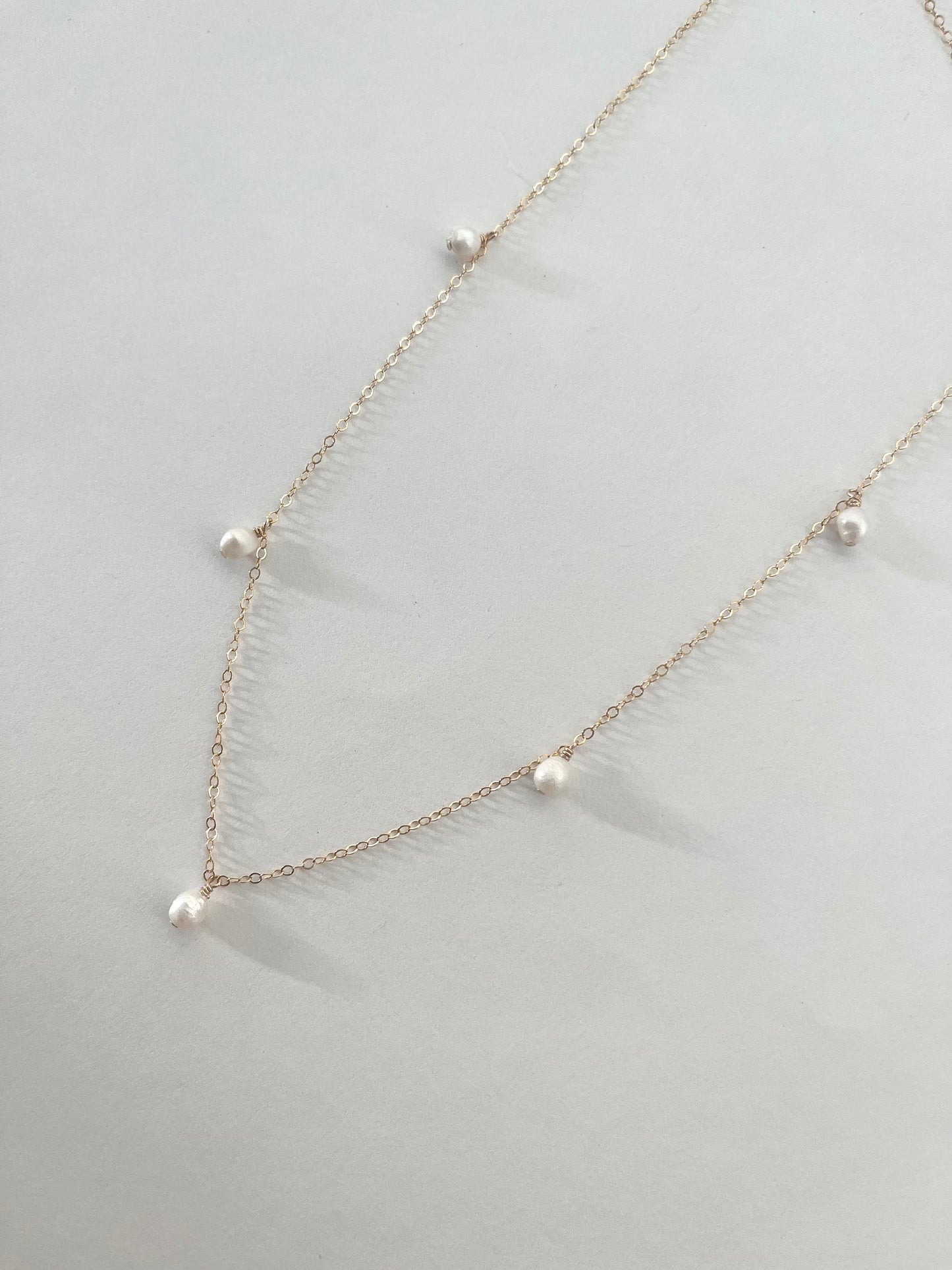 14k gold filled cable chain necklace with five small fresh water pearls laying flat against a white background